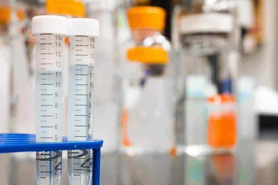 Two test tubes filled with Ammonia sit on a lab countertop, with other lab equipment blurred in the background.
