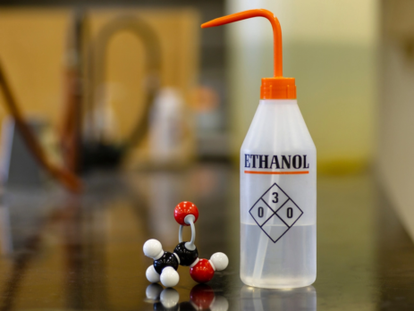 Bottle of ethanol on table next to 3D molecular structure