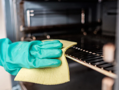 Gloved hand cleaning oven rack with yellow sponge