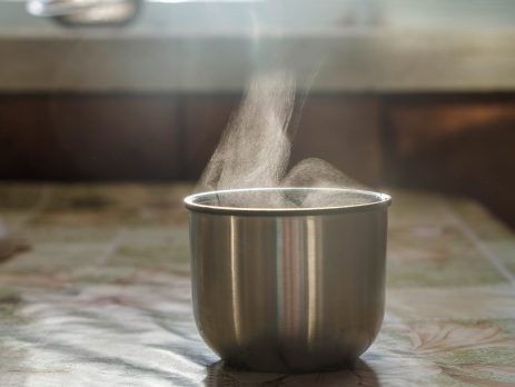 Metal thermos cup on tabletop with steam rising from it