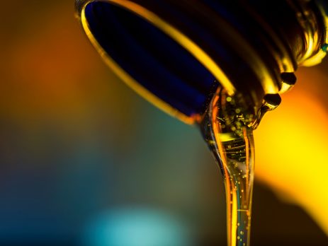 Liquid stream of motor oil flows from the neck of the bottle close-up.