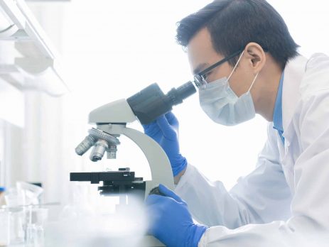 Science technician looking through microscope