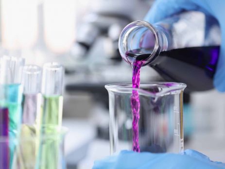 Scientist chemist pouring pink liquid into test tube in lab closeup