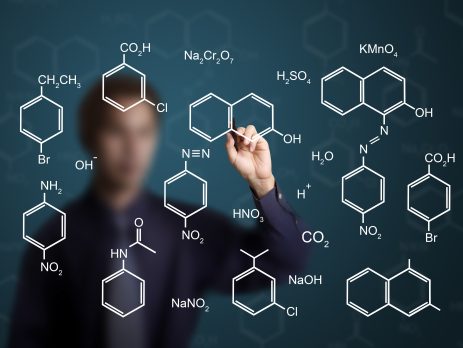 Teacher writing different organic and inorganic chemistry formulas on reversible mirror wall