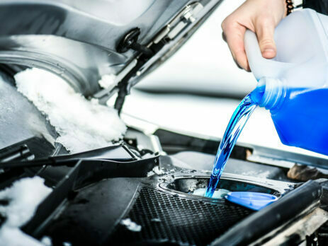 A person pouring blue antifreeze into a car engine for the window screen.