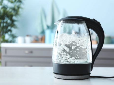 Transparent electric kettle with boiling water on a table in a kitchen