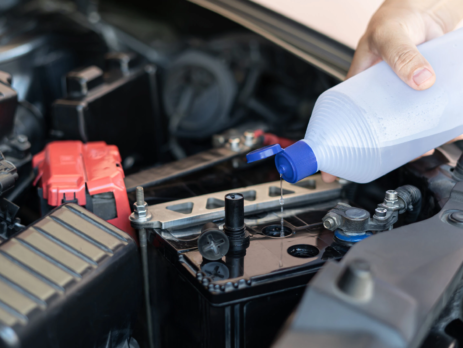 Person adding distilled water from a bottle to a car battery
