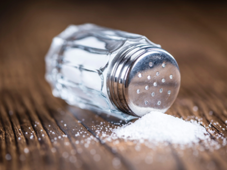 Salt shaker knocked over with salt spilling onto a wooden table