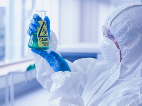 Close-up side view of a scientist in protective suit looking at hazardous blue chemical