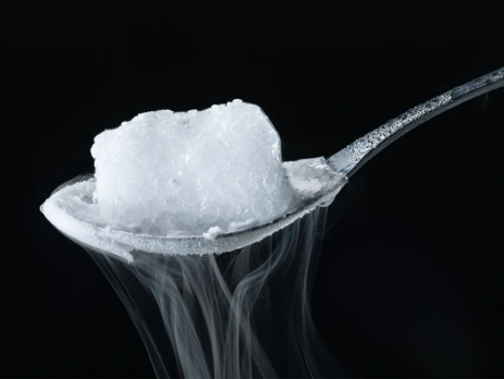 A cube of dry ice, an example of an exothermic reaction, sublimates on a silver spoon against a black background.