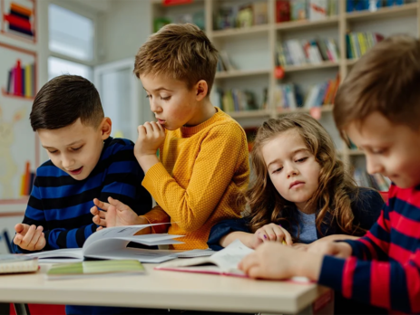 A group of children in colourful jumpers reading science books in a classroom.